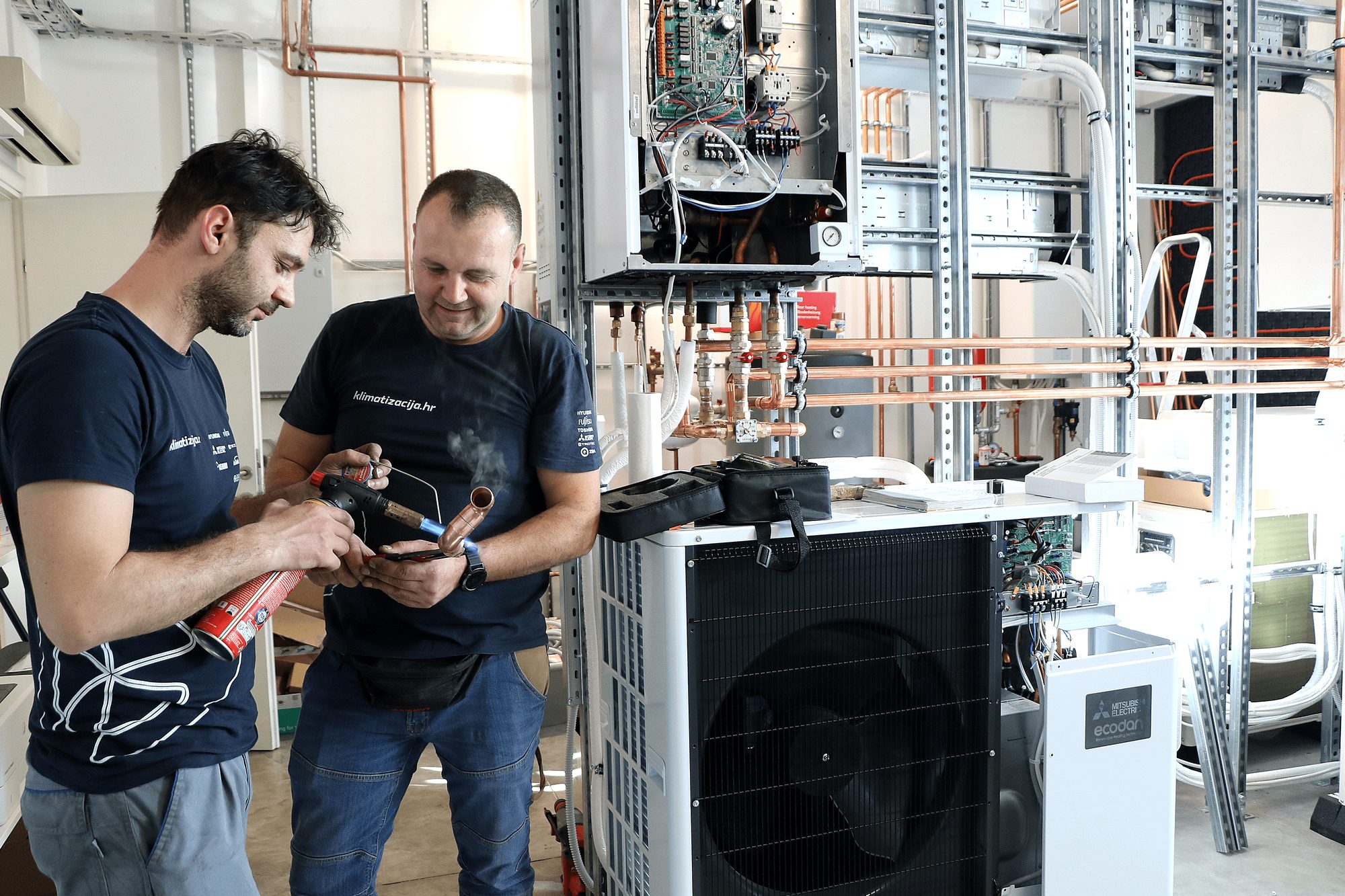 Dva instalatera s plamenikom i bakrenom cijevi uz Mitsubishi Electric Ecodan dizalicu topline
